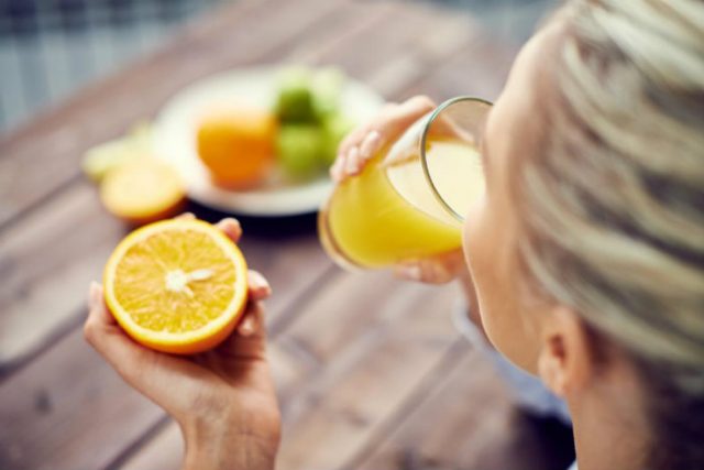 a-woman-drinking-orange-juice-and-holding-an-orange-vitamins