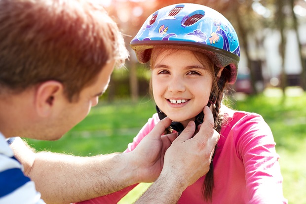 picture of father helping his daughter  with hear helmet in a park