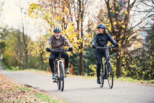 woman and elderly man riding electric cycles in the forest 