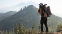 Female hiker stands on rock looking at the horizon witk backpack