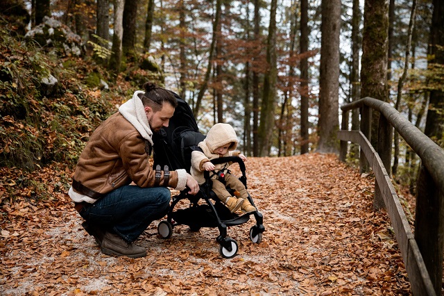 picture of a men with a baby in a stroller in a mountain path with brown leaves  