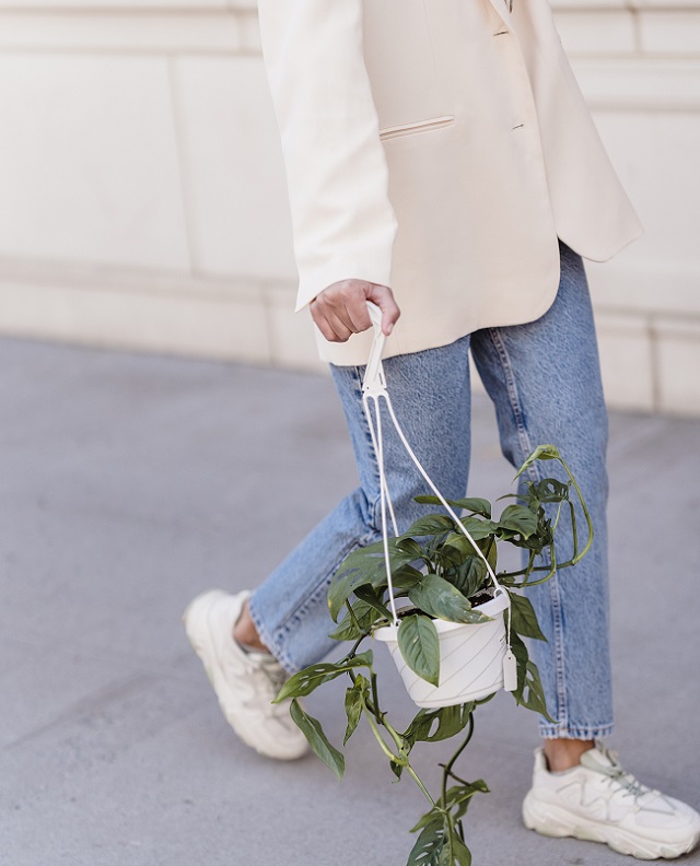 picture of a woman walking on a sidewalk wearing sneaker, jeans and a jacket holding a flowerpot