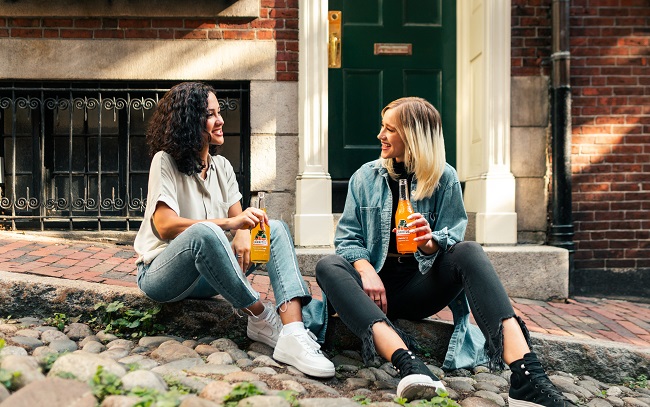 picture of two women sitting on the sidewalk with soda in their hands 