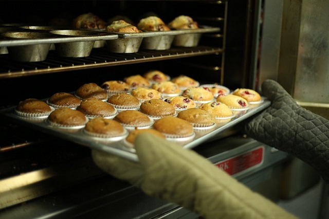 picture of a person holding baked muffins out of a bakery oven 