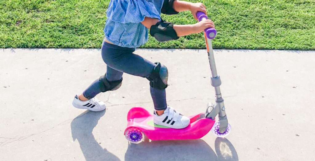 little girl riding a scooter with knee and elbow pads