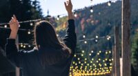 young woman is dancing against the backdrop of mountains, cozy light bulbs for a festival atmosphere.